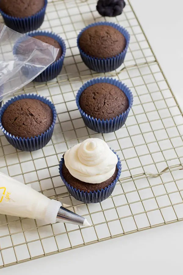 One chocolate cupcake with marshmallow frosting on a cooling rack.