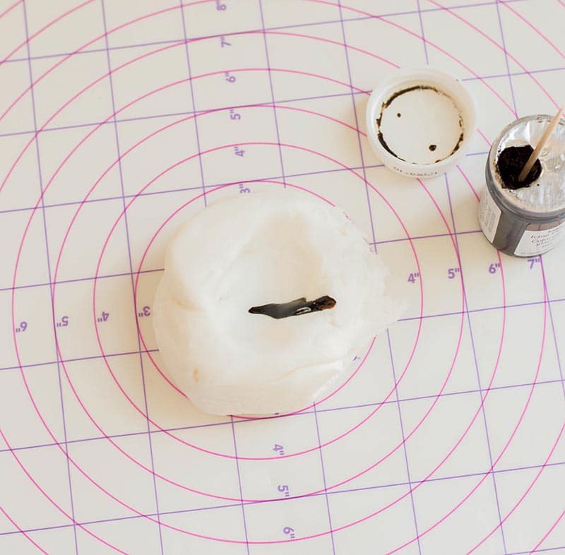 Brown gel food coloring added to ball of white fondant on pastry mat.