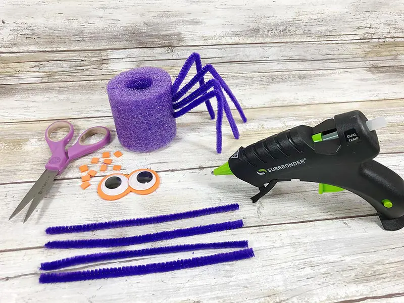 Supplies for pool noodle spider on light wood background. Half of pipe cleaners inserted in pool noodle for spider legs.