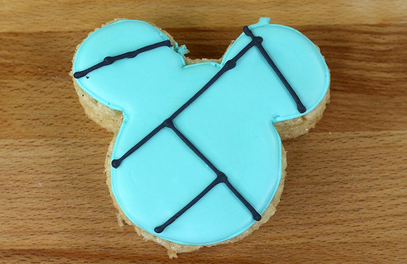 Rice crispy shaped like Mickey with teal icing on top and black lines to show how to make stitch marks for decoration.