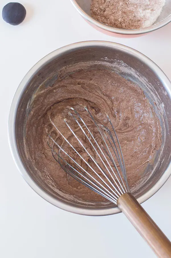 Whisking dry ingredients to chocolate cupcake batter in silver mixing bowl.