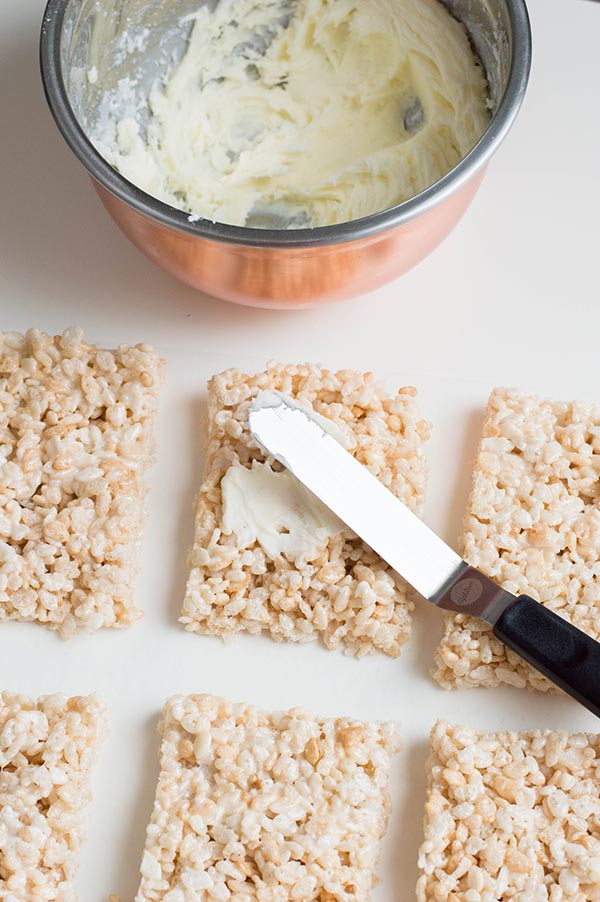 Spreading buttercream icing on rice crispy treats with offset spatula.