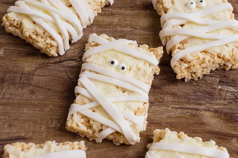 Close up of a few mummy decorated rice crispy treats on table.