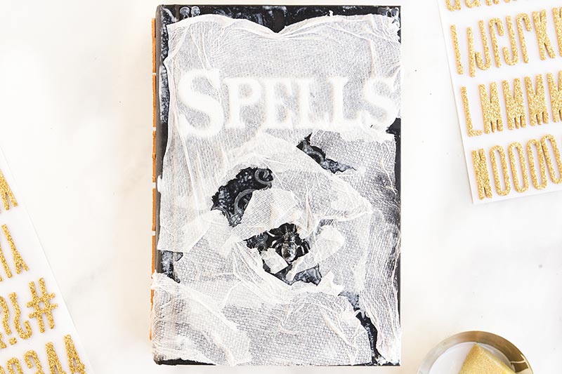 Ripped pieces of paper towel covering hardcover book with mod podge on white table