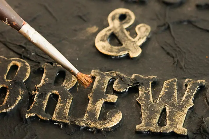 Close up of paint brush painting letters gold for diy spell book