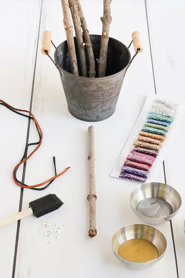 Sticks in a silver bucket and other supplies for wand craft on a white table.