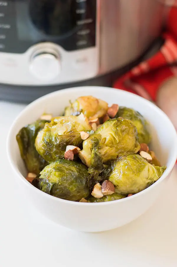 Brussels sprouts in small white bowl in front of pressure cooker.