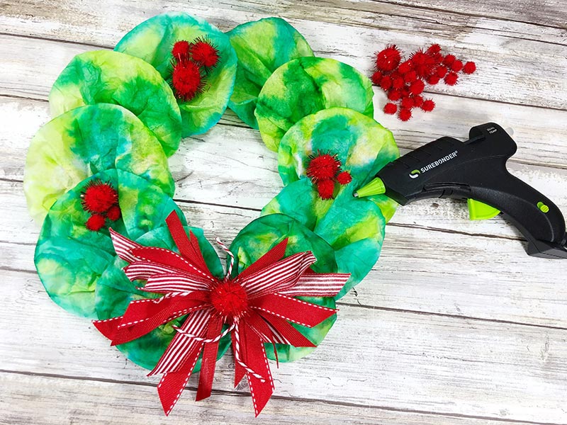 Hot gluing red pom poms onto coffee filter wreath.