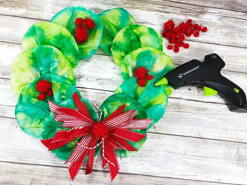 Hot gluing red pom poms onto coffee filter wreath.