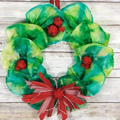 Christmas wreath made with coffee filters hanging in front of white wood backdrop.