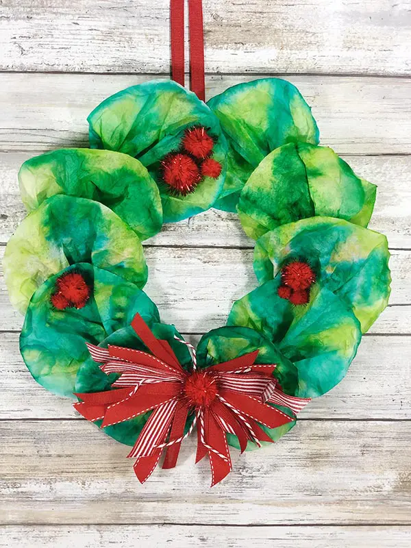 Christmas wreath made with coffee filters hanging in front of white wood backdrop.