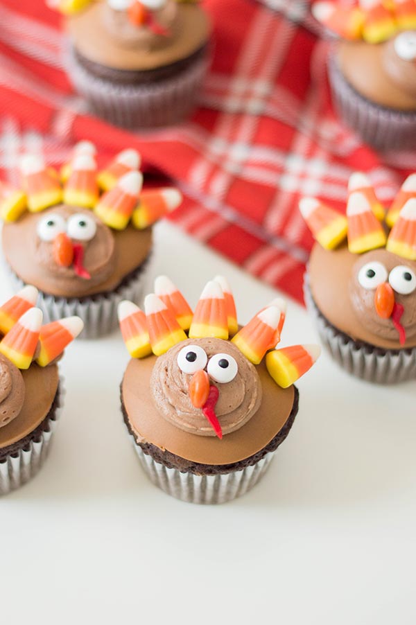 Cupcakes decorated like turkeys on white counter and red plaid cloth.