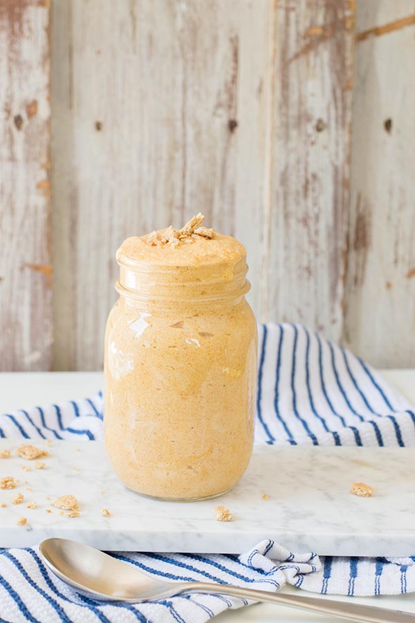 Pumpkin mousse in mason jar on small white serving tray. Tray set on blue and white striped kitchen towel with spoon next to it.