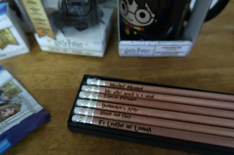 Set of six pencils with Harry Potter phrases laser engraved on them in a black box. Pencil set sitting on table by a mug.