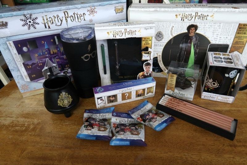 Harry Potter advent calendar, mugs, tumbler, pencils, invisibility cloak, diary, keychain, and kblings arranged on top of table.