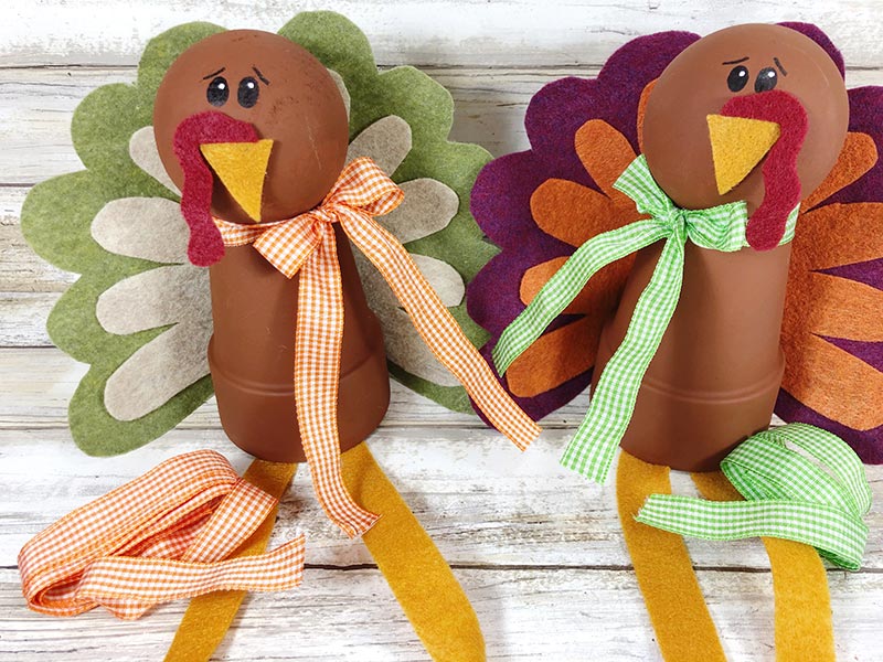 Two finished turkey clay pot projects sitting side by side with gingham green and gingham orange ribbons tied around the neck.