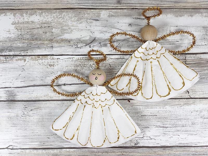 Two finished angel ornaments, one with painted face and one with blank face on white wood background.