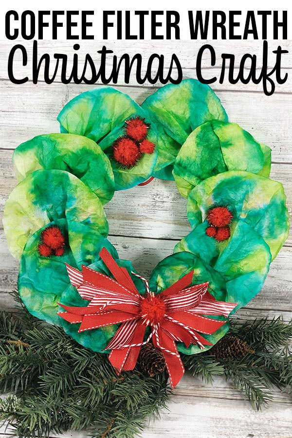 Coffee filter wreath propped up on sprig of evergreen on a white wood background.