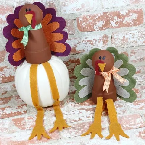 Two completed turkeys made with flower pots and felt feathers on light brick background.