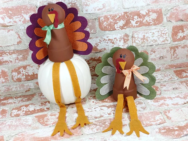 Two completed turkeys made with flower pots and felt feathers on light brick background.