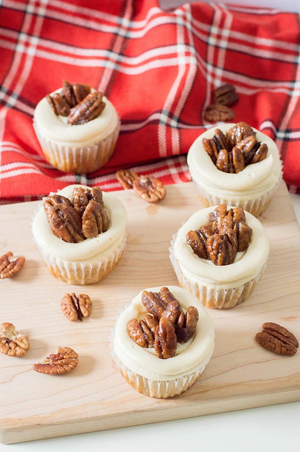 Five cupcakes topped with pecans on a wood cutting board and red flannel cloth.