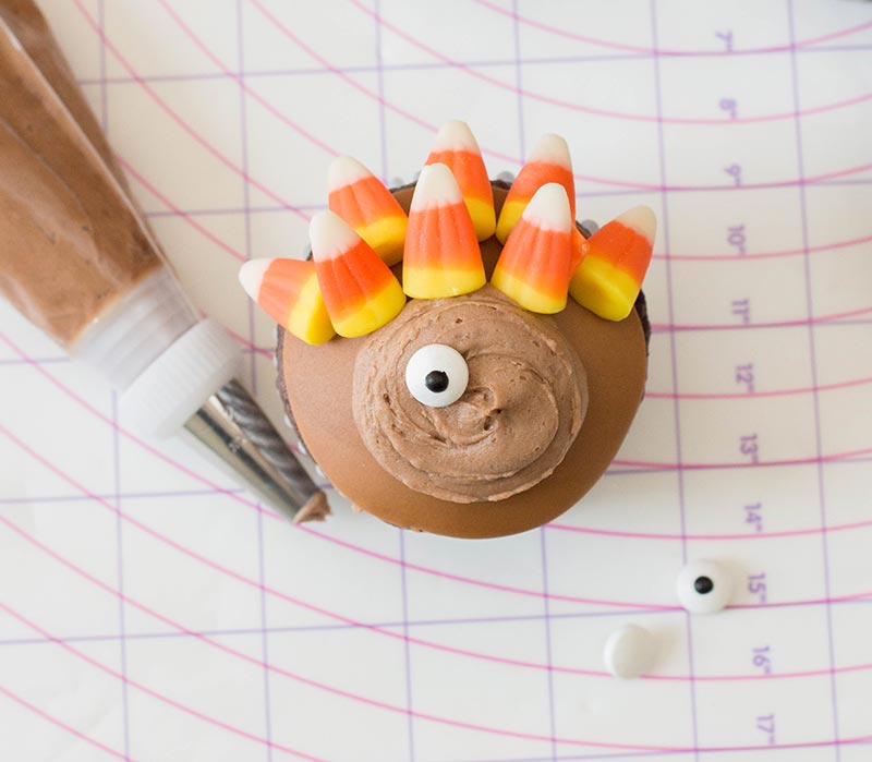 Cupcake being decorated with fondant, candy corn, buttercream, and a candy eye.