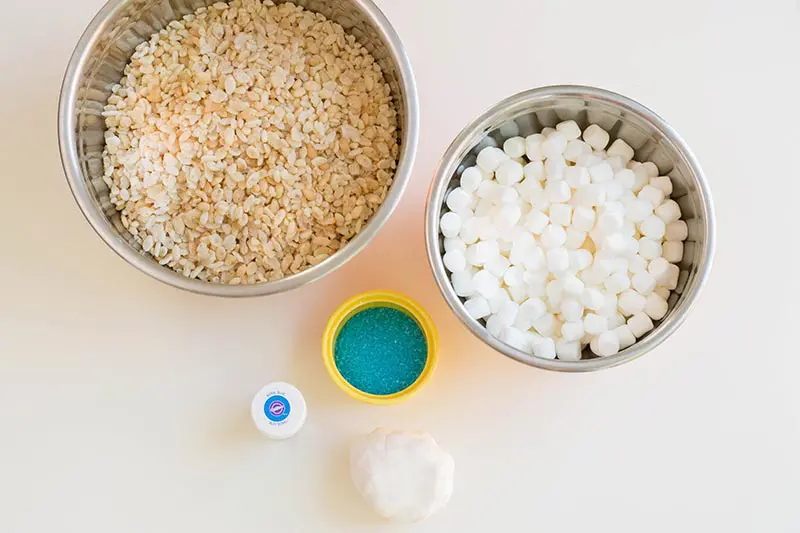 Ingredients for Elsa decorated rice crispy treats in bowls on white table.