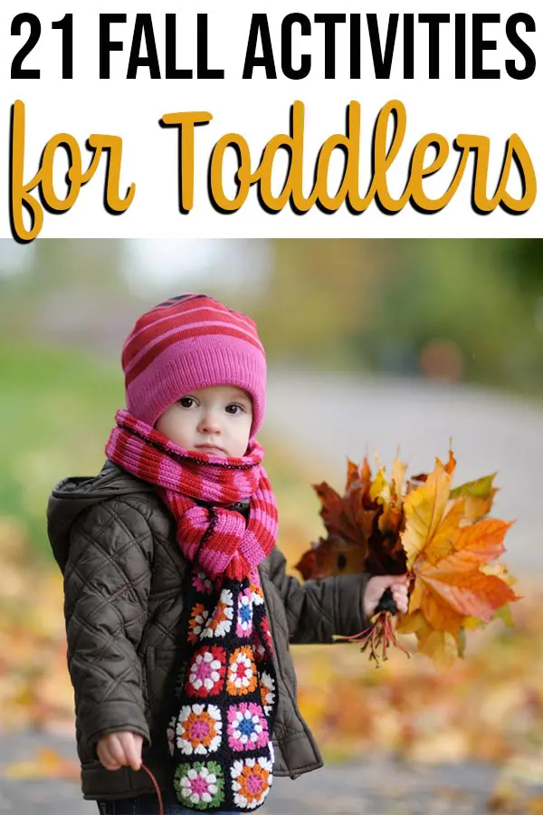 Toddler wearing pink hat, scarf, and coat holding a handful of fall leaves.