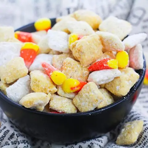 Small black bowl full of fall puppy chow chex mix with candy corn.