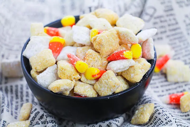 Small black bowl full of fall puppy chow chex mix with candy corn.