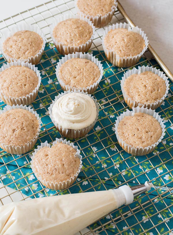 One frosted cupcake and several unfrosted cupcakes on wire rack by piping bag.