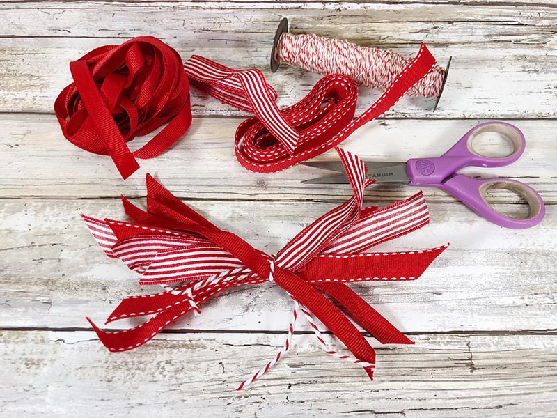 Tying twine around scraps of red and white ribbon pieces to create a bow.