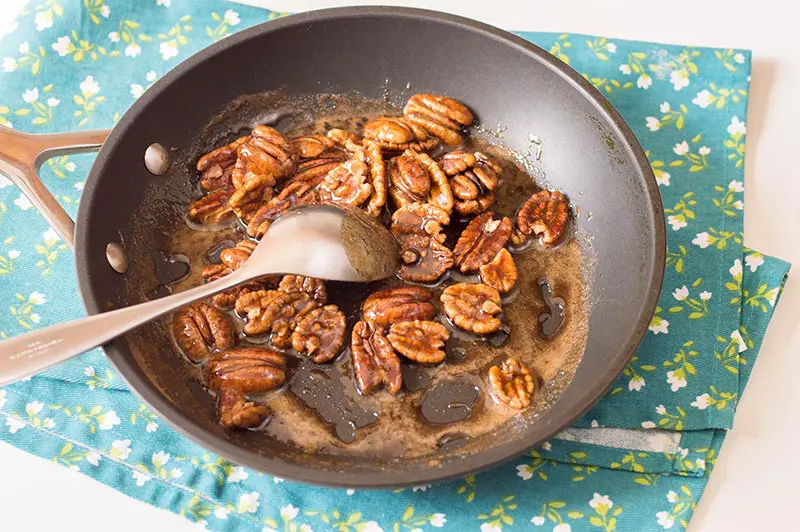 Stirring pecans in brown sugar mixture in a pan.