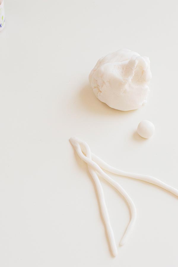 Braiding strips of white fondant on white tabletop.