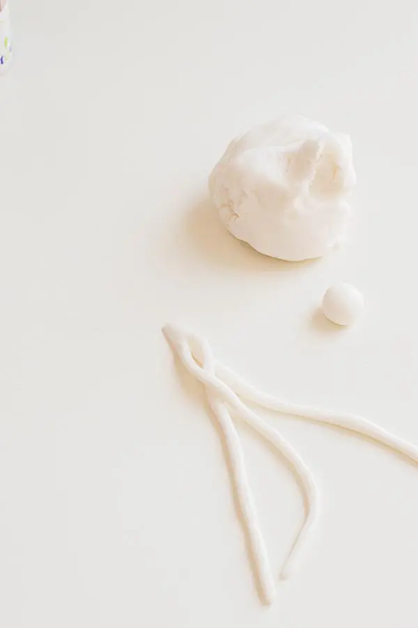 Braiding strips of white fondant on white tabletop.