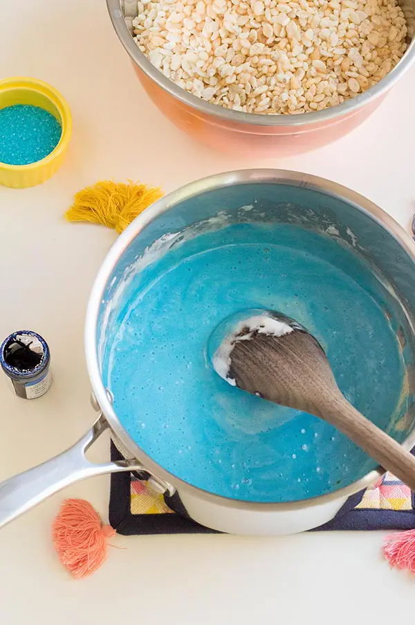 Mixing blue gel food coloring into melted marshmallows in pot.