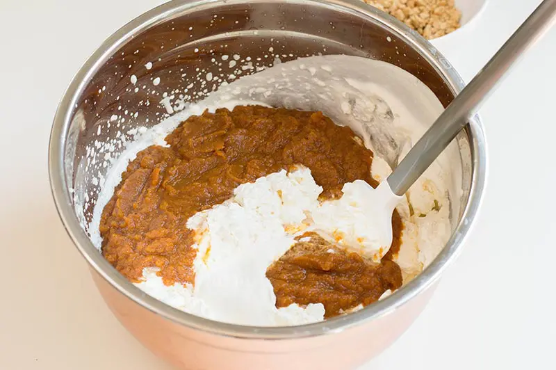 Folding whipped heavy cream into pumpkin puree mixture with spatula.