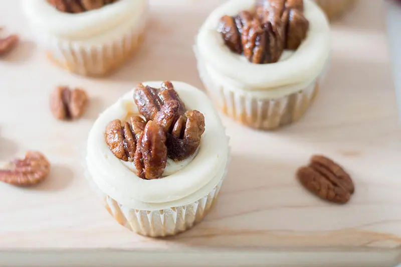 Close up of frosted cupcakes with candied pecans on top.