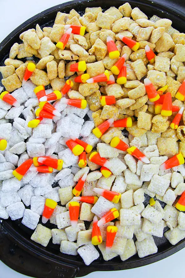 Homemade fall puppy chow recipe with candy corn on a black tray.
