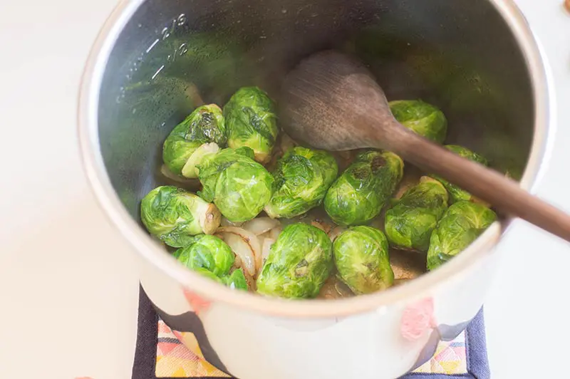 Brussels sprouts and onions and wooden spoon in silver pot.