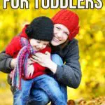 Mom hugging smiling toddler outside while kneeling in pile of leaves. Text overlay at top says 21 fall activities for toddlers.