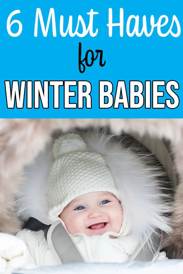 Smiling baby wearing a white winter hat and white coat.