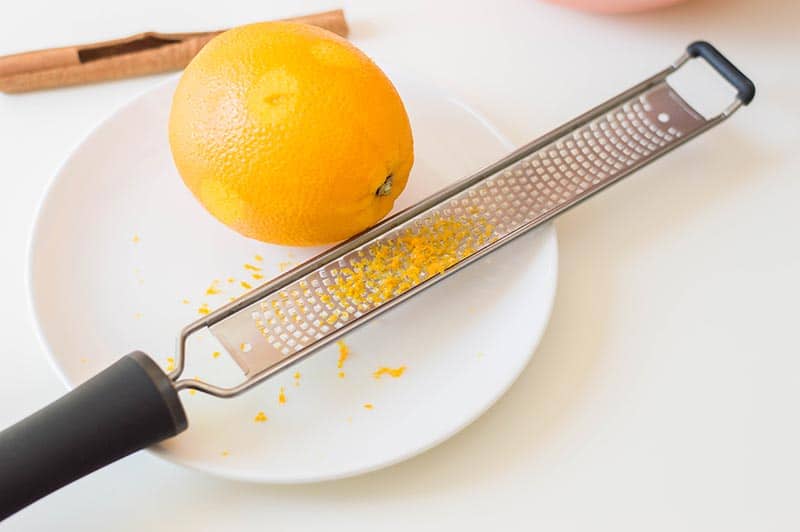 Partially zested orange on small white plate next to zest grater.