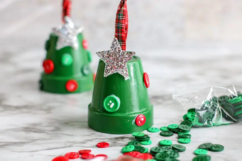 Gluing red and green buttons and glittery silver star to green painted clay pots.