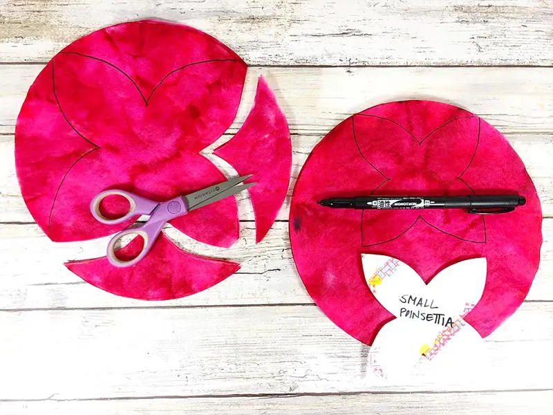 Tracing poinsettia flower template on red coffee filters and cutting them out.