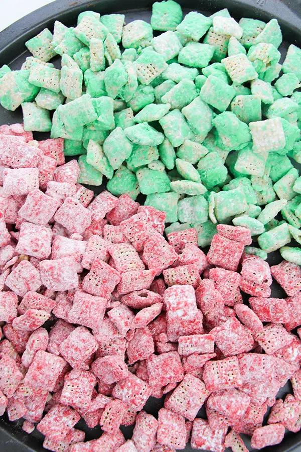 Red and green coated Chex cereal spread out on baking sheet. Colors are separated, red on left and green on right.