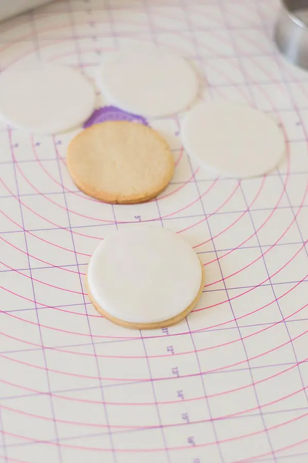 Round sugar cookie and round white fondant cut outs on pastry mat. One fondant circle is on top of a sugar cookie.