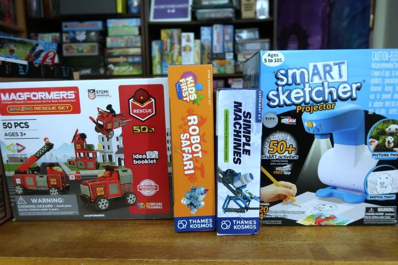 Magformers fire truck set, Robot Safari kit, Simple Machines kit, and smART sketch projector boxes sitting side by side on my table.
