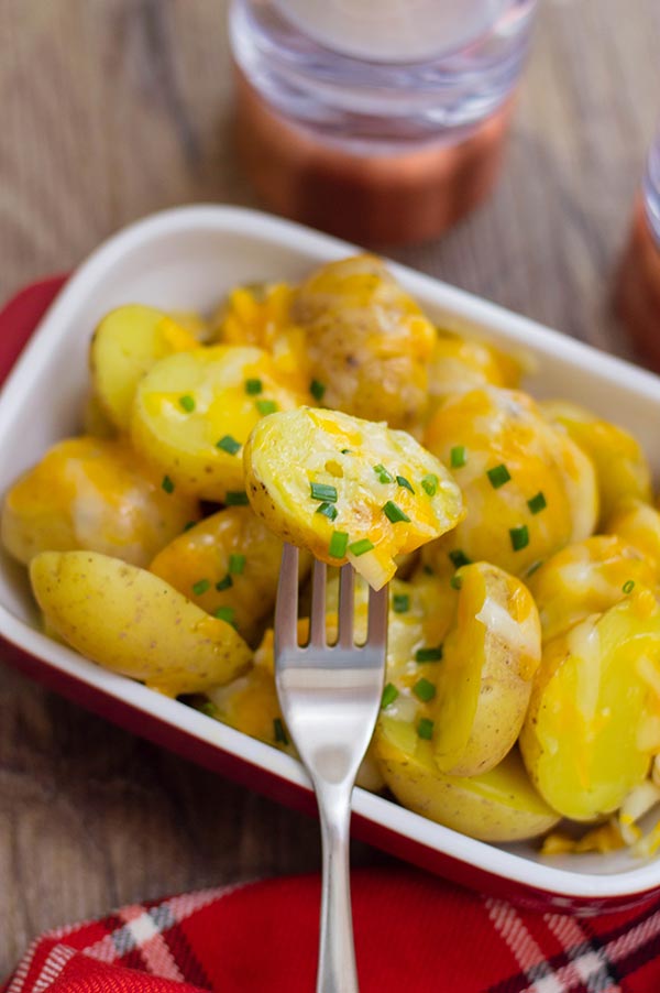 Forkful of cheesy potatoes resting on serving dish with more potatoes.