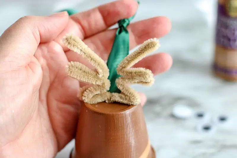 Two tan pipe cleaners shaped like antlers attached to top of clay pot to make reindeer.